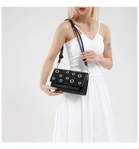 Detail of black glossy leather crossbody bag with silver eyelet studs and shoulder strap