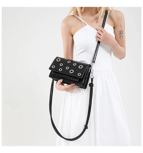 Detail of black punk crossbody bag with metallic silver eyelets on the rectangular flap