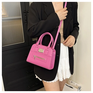 Close-up of a pink glossy mini handbag with metallic branding plate and shoulder strap