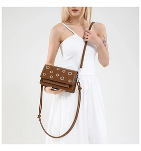 Close-up of brown leather crossbody bag with metallic eyelets worn by a model