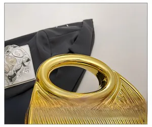 Detail of gold crescent evening bag with hollow handle and vertical stripe metal finish