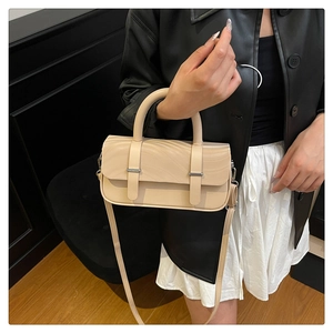 Close-up of a beige box crossbody bag with silver hardware on a leather jacket outfit