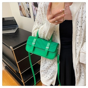 Detail of a bright green crossbody box bag featuring textured flap and silver metal buckles