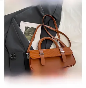 Detail of a brown matte leather box bag with cylindrical handle on a stylish blazer background