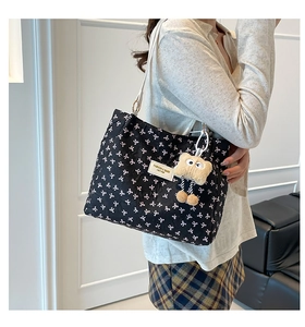 Detail of black bow print tote bag with white leather strap and plush toy charm on model