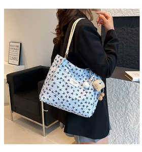 Detail of light blue quilted tote bag with black bow embroidery and plush pendant