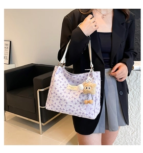 Dettaglio della borsa tote lavanda con motivi a fiocco viola e ciondolo di peluche sulla tracolla