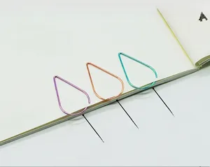Detail of colorful water drop shaped metal paperclips in purple, orange, and cyan on a notebook