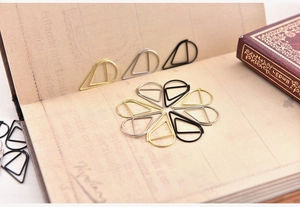 Macro shot of gold silver and black teardrop paper clips arranged on a vintage notebook