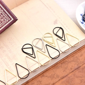 Minimalist teardrop metal paperclips in gold, silver, and black on a vintage notebook