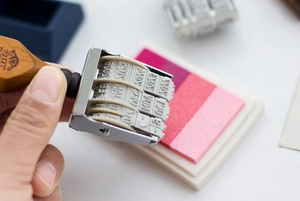 Close-up of vintage wooden date stamp with metal frame and rubber rollers on ink pad