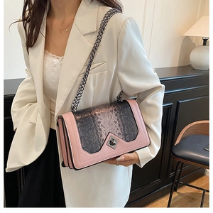 Model wearing a pink faux leather crossbody bag with snake print detail and silver chain