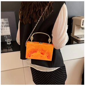 Detail of a bright orange marble acrylic box bag with a gold handle and chain strap