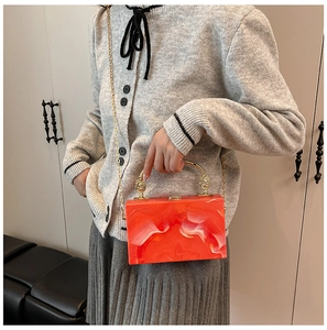 Detail of orange marble acrylic evening bag with gold handle on a neutral background