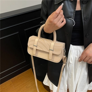 Beige box crossbody bag with unique textured flap and dual buckle straps on dark background