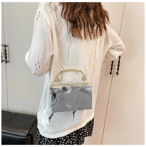 Detail van grijze marmeren acryl boxclutch met goudkleurig metalen handvat en fijne ketting