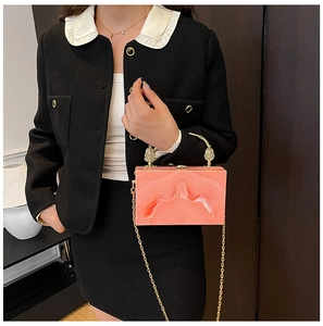 Detail van marmerpatroon acryl clutch tas met gouden leeuw sieraad en kettingriem