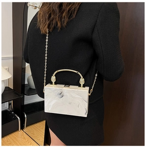 Detail van marmeren acryl box clutch met gouden handvat en ketting op een tweed jasje