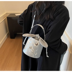 Detail of silver bucket bag featuring metal butterfly charm and rabbit ear drawstrings