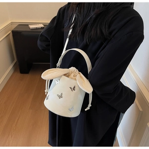 White bucket bag with silver butterfly charm and rabbit ear drawstring closure