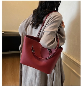 Close-up of red litchi leather tote bag with fine stitching and golden brand logo detail