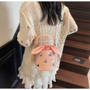 Detail view of pink bucket bag with silver butterfly charms and rabbit ear drawstring