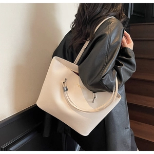Close-up of white leather tote bag with lychee texture and gold letter logo on shoulder