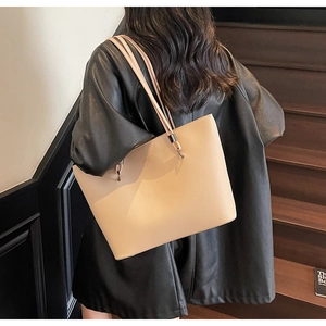 Close-up of beige tote bag in lychee pattern leather held by a model on stairs