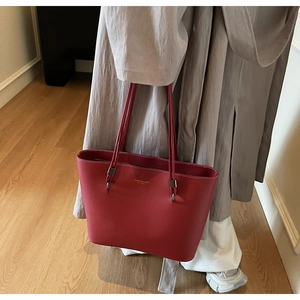 Detail of red leather tote bag with gold logo being carried by model in casual setting