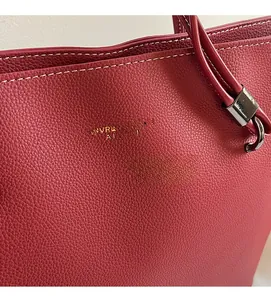 Detail of red lychee leather tote bag with white contrast stitching and gold logo
