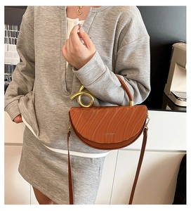Fashionable brown leather saddle bag with twisted gold handle shown in a lifestyle scene