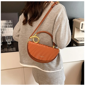 Detail of a brown half-moon bag featuring pleated texture and a gold metal ring handle