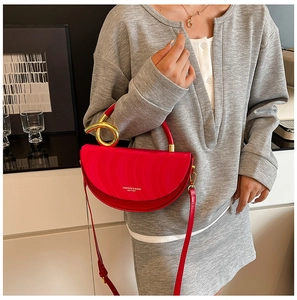 Red semi-circular crossbody bag with golden handle shown on model in a modern room
