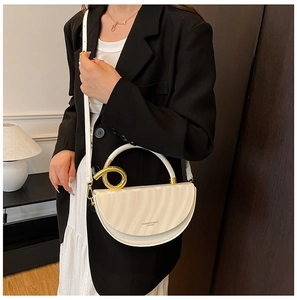 Detail of cream half-moon crossbody bag with gold twisted metal hardware on a model