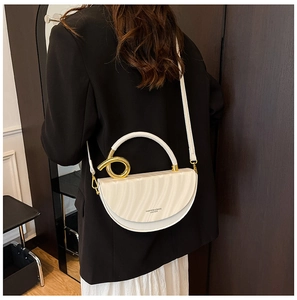 Detailed view of white leather saddle bag with gold ring handle and wavy texture