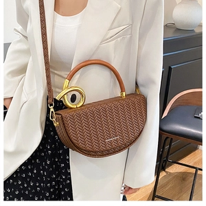 Détail d'un sac selle marron à texture tressée avec anneau doré et poignée