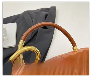 Detail of brown leather handle with golden metal rings and wave texture on the box bag
