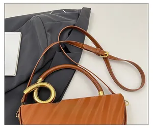 Detail of a brown leather box bag with a golden circular metal handle and shoulder strap
