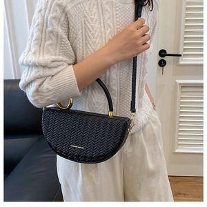 Détail du sac demi-lune tressé noir avec ferrures dorées et texte de mode gravé