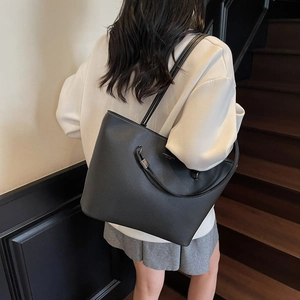 Retro black leather tote bag with white stitching shown on shoulder in indoor scene