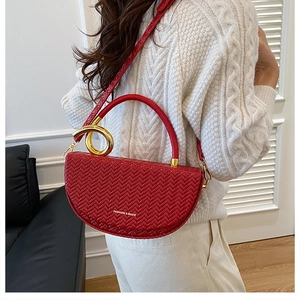 Détail de la texture tressée du sac selle rouge avec anneau métallique doré élégant