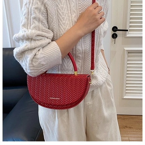 Détail du sac bandoulière rouge à texture tressée avec texte mode et boucles métalliques dorées