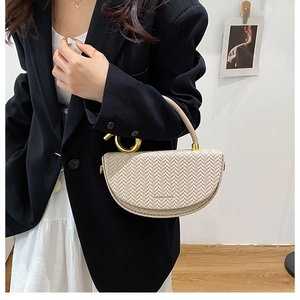 Détail du sac à main beige tressé avec anneau doré porté par un mannequin en tenue chic
