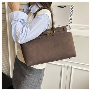 Detail view of large brown tote bag with metal buckle decor and protective bottom rivets