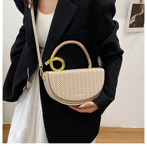 Détail d'un sac demi-lune tressé crème avec anneaux dorés porté par un mannequin