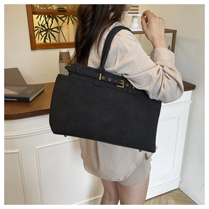 Detail of a black matte leather tote bag featuring gold buckles and studs in a cafe setting