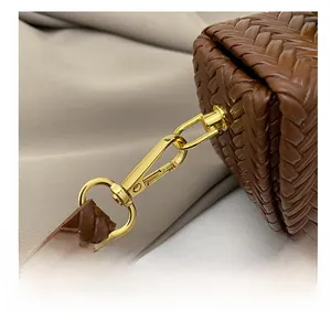 Gros plan sur les ferrures dorées et le cuir tressé complexe d'un sac à main marron