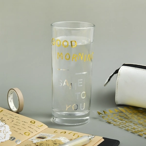 Minimalist clear glass cup with gold Good Morning typography on a creative desk setting