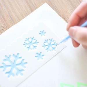 Hollow snowflake stencils for drawing with a blue pen on white paper and wood