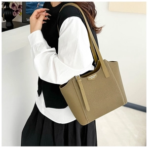 Detail of a dark green leather tote bag with a fashion shield logo and slim strap